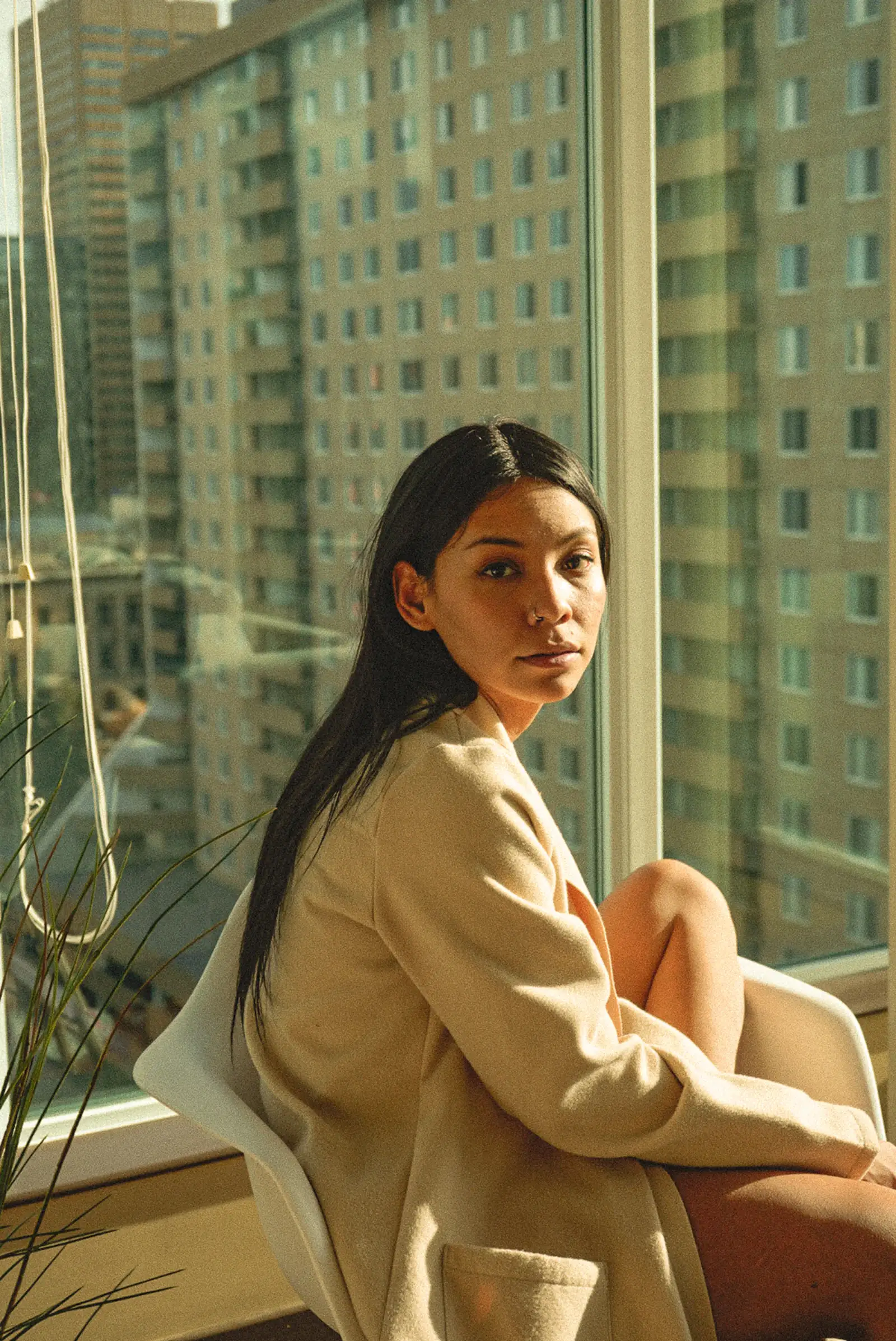 Woman in a beige blazer sitting by a tall window in soft city light